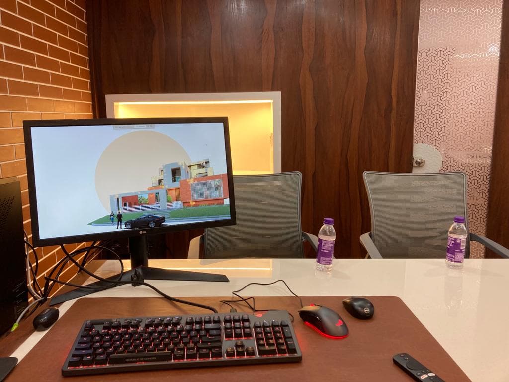 Inside the MRS Architects studio — a desk workstation with a residential render on the monitor, set against a brick and rosewood wall with a patterned feature panel beyond.